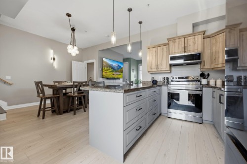 Contemporary kitchen featuring a central island with grey cabinetry, granite countertops, stainless steel appliances, wood-finish flooring, and pendant lighting - #201 10625 Kingsway Av Nw, Edmonton, AB - Indoor Photo Showing Kitchen