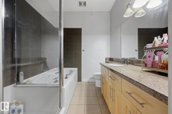 Bathroom featuring a combined tub and shower enclosure with glass panels, a long vanity with light wood-finish cabinetry, a single basin sink, and a speckled countertop - 