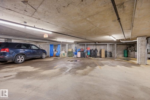 Underground parking area featuring a concrete floor and ceiling, exposed conduit, fluorescent lighting, and chained storage units - #201 10625 Kingsway Av Nw, Edmonton, AB - Indoor Photo Showing Garage