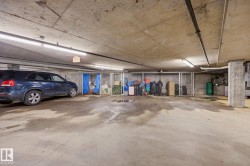 Underground parking area featuring a concrete floor and ceiling, exposed conduit, fluorescent lighting, and chained storage units - 