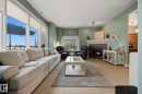 Spacious living area featuring large windows with roller shades, light wood-finish flooring, and a built-in fireplace with a stone surround and wood mantel - #201 10625 Kingsway Av Nw, Edmonton, AB  - Indoor Photo Showing Living Room With Fireplace 