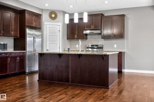 Spacious kitchen featuring dark wood cabinetry, a large center island with a speckled countertop, and wood-finish flooring - 3639 15A Street Nw, Edmonton, AB - Indoor Photo Showing Kitchen