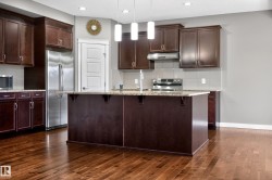 Spacious kitchen featuring dark wood cabinetry, a large center island with a speckled countertop, and wood-finish flooring - 
