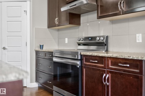 Contemporary kitchen featuring stainless steel appliances, a range hood, dark wood cabinetry, light-toned tile backsplash, and granite countertops - 3639 15A Street Nw, Edmonton, AB - Indoor Photo Showing Kitchen
