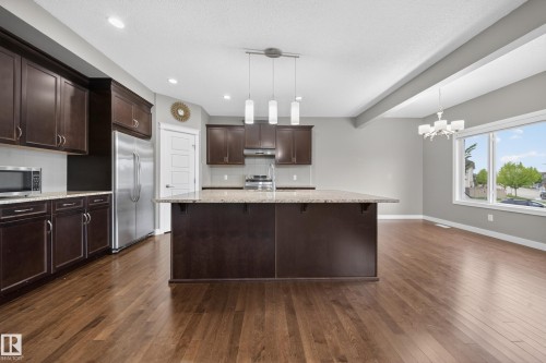 Spacious kitchen featuring rich wood-finish cabinetry, a large center island with a light-toned countertop, stainless steel appliances, and wood-finish flooring - 3639 15A Street Nw, Edmonton, AB - Indoor Photo Showing Kitchen