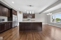 Spacious kitchen featuring rich wood-finish cabinetry, a large center island with a light-toned countertop, stainless steel appliances, and wood-finish flooring - 