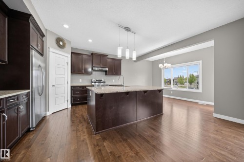 Kitchen featuring dark wood cabinetry, stainless steel appliances, granite countertops, and a central island with pendant lighting - 3639 15A Street Nw, Edmonton, AB - Indoor Photo Showing Kitchen With Upgraded Kitchen