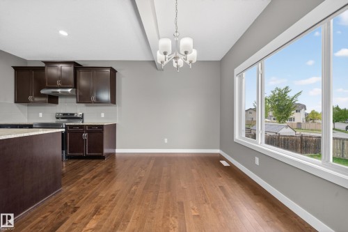Open-concept living area featuring rich wood-finish flooring, a contemporary chandelier, large picture windows, a full kitchen with dark cabinetry, and light-toned countertops - 3639 15A Street Nw, Edmonton, AB - Indoor Photo Showing Kitchen
