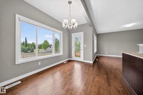 Spacious room featuring wood-finish flooring, a contemporary chandelier, and a large window with white trim - 3639 15A Street Nw, Edmonton, AB - Indoor Photo Showing Other Room