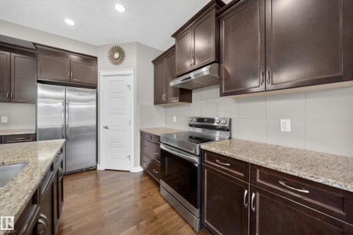 Kitchen featuring dark wood cabinetry, stainless steel appliances, granite countertops, wood-finish flooring, and recessed lighting - 3639 15A Street Nw, Edmonton, AB - Indoor Photo Showing Kitchen With Upgraded Kitchen