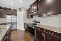 Kitchen featuring dark wood cabinetry, stainless steel appliances, granite countertops, wood-finish flooring, and recessed lighting - 
