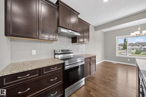 Kitchen featuring dark wood cabinetry, light speckled countertops, stainless steel range with overhead ventilation, and a white tile backsplash - 3639 15A Street Nw, Edmonton, AB - Indoor Photo Showing Kitchen