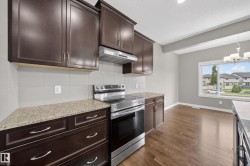 Kitchen featuring dark wood cabinetry, light speckled countertops, stainless steel range with overhead ventilation, and a white tile backsplash - 