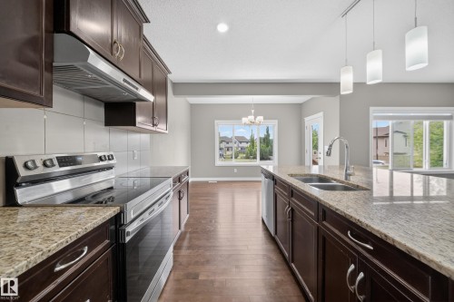 Spacious kitchen featuring rich wood cabinetry, stainless steel appliances, light-colored stone countertops, and wood-finish flooring - 3639 15A Street Nw, Edmonton, AB - Indoor Photo Showing Kitchen With Double Sink With Upgraded Kitchen