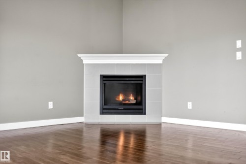 Corner fireplace with a white mantel, light gray tile surround, and black firebox - 3639 15A Street Nw, Edmonton, AB - Indoor Photo Showing Living Room With Fireplace