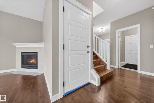 Living area with wood-finish flooring, a fireplace featuring a tile surround and white mantel, and neutral wall tones - 3639 15A Street Nw, Edmonton, AB - Indoor Photo Showing Other Room