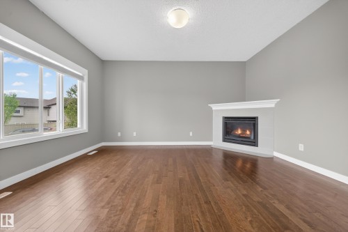 Spacious room featuring wood-finish flooring, a contemporary fireplace with a white mantel, and a large window with white trim - 3639 15A Street Nw, Edmonton, AB - Indoor Photo Showing Living Room With Fireplace