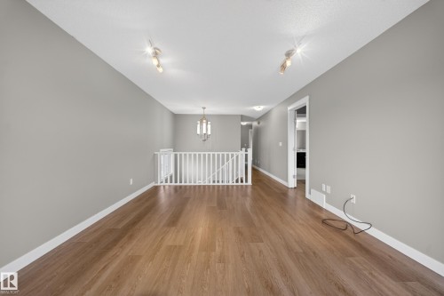 Spacious room featuring wood-finish flooring, light grey walls, white trim, and a white railing - 3639 15A Street Nw, Edmonton, AB - Indoor Photo Showing Other Room