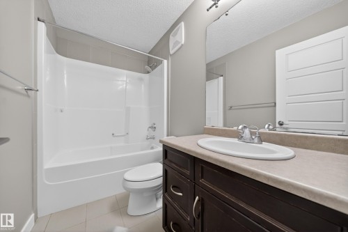 Bathroom featuring a dark wood-finish vanity with an integrated sink, a large wall-mounted mirror, a tub/shower combination with a shower rod, and light-toned tile flooring - 3639 15A Street Nw, Edmonton, AB - Indoor Photo Showing Bathroom