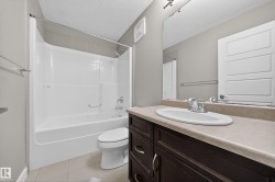 Bathroom featuring a dark wood-finish vanity with an integrated sink, a large wall-mounted mirror, a tub/shower combination with a shower rod, and light-toned tile flooring - 