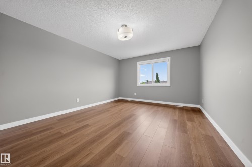 Spacious interior featuring wood-finish flooring, a contemporary ceiling light fixture, and a window with white trim - 3639 15A Street Nw, Edmonton, AB - Indoor Photo Showing Other Room