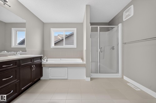 Spacious bathroom featuring a double vanity with dark wood cabinetry, a built-in bathtub, a stand-up shower with a glass enclosure, and light-colored tile flooring - 3639 15A Street Nw, Edmonton, AB - Indoor Photo Showing Bathroom