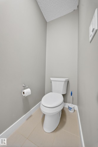 Powder room featuring a white toilet, light gray painted walls, textured ceiling, light-toned tile flooring, and white baseboards - 3639 15A Street Nw, Edmonton, AB - Indoor Photo Showing Bathroom