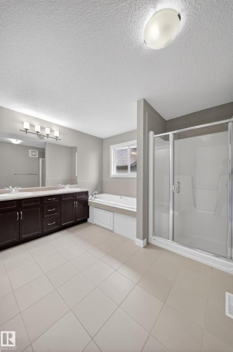 Spacious bathroom featuring tiled flooring, a dual-sink vanity with dark wood cabinetry, a built-in soaking tub, and a glass-enclosed shower - 3639 15A Street Nw, Edmonton, AB - Indoor Photo Showing Bathroom