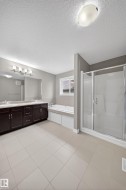 Spacious bathroom featuring tiled flooring, a dual-sink vanity with dark wood cabinetry, a built-in soaking tub, and a glass-enclosed shower - 