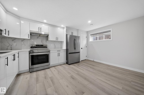Modern kitchen featuring white cabinetry, stainless steel appliances, a white marble-look backsplash, light wood-finish flooring, and recessed lighting - 3639 15A Street Nw, Edmonton, AB - Indoor Photo Showing Kitchen