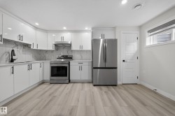 Modern kitchen featuring white cabinetry with matte black hardware, stainless steel appliances, a marble-look backsplash, light wood-finish flooring, and recessed lighting - 