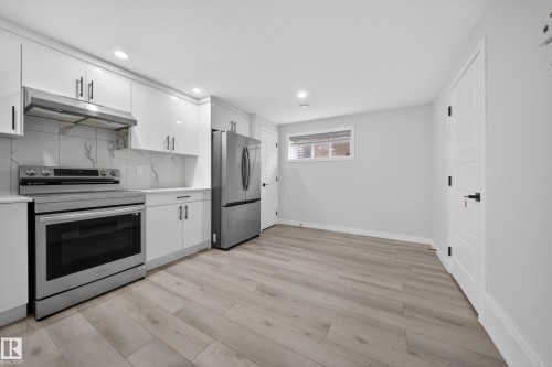 Contemporary kitchen featuring white cabinetry, stainless steel appliances, marble-look backsplash, and light wood-finish flooring - 3639 15A Street Nw, Edmonton, AB - Indoor Photo Showing Kitchen