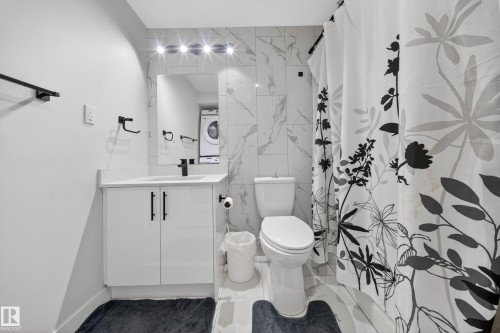 Bathroom featuring a white vanity with a solid surface countertop, matte black fixtures, a wall-mounted mirror, and white tile flooring - 3639 15A Street Nw, Edmonton, AB - Indoor Photo Showing Bathroom