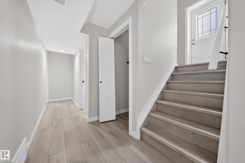 Entryway featuring wood-finish flooring, a contemporary staircase with white risers and railing, and a white entry door with decorative glass - 3639 15A Street Nw, Edmonton, AB - Indoor Photo Showing Other Room