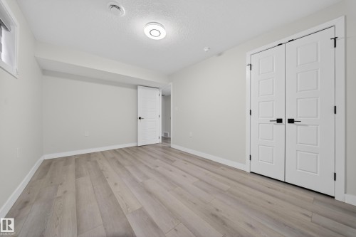 Spacious room featuring light wood-finish flooring, white baseboards, and a pair of contemporary panel doors with black hardware - 3639 15A Street Nw, Edmonton, AB - Indoor Photo Showing Other Room