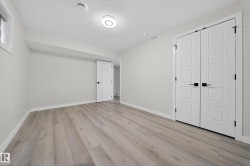 Spacious room featuring light wood-finish flooring, white baseboards, and a pair of contemporary panel doors with black hardware - 