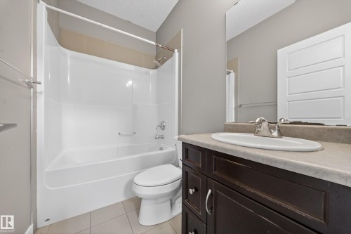 Full bathroom featuring a dark wood-finish vanity with a light countertop, an integrated sink with a chrome faucet, and a large mirror - 3639 15A Street Nw, Edmonton, AB - Indoor Photo Showing Bathroom