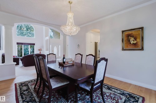 Formal dining space featuring a prominent crystal chandelier, light wood-finish flooring, and crown molding - 928 Heacock Road Nw, Edmonton, AB - Indoor Photo Showing Dining Room