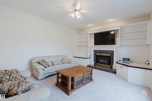 Living room featuring a central fireplace with a dark stone surround and white mantel, flanked by built-in shelving and cabinetry - 928 Heacock Road Nw, Edmonton, AB - Indoor Photo Showing Living Room With Fireplace