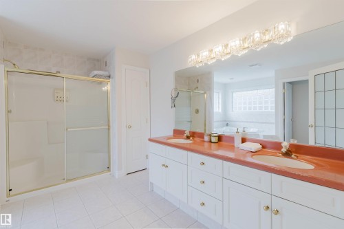 Spacious bathroom featuring a dual vanity with a coral-toned countertop, a large mirror, and an ornate crystal light fixture - 928 Heacock Road Nw, Edmonton, AB - Indoor Photo Showing Bathroom