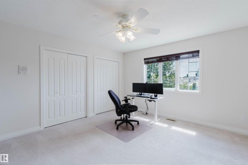 Carpeted room featuring a ceiling fan with integrated lighting, a large window with horizontal blinds, and two sets of bi-fold closet doors - 928 Heacock Road Nw, Edmonton, AB - Indoor Photo Showing Office