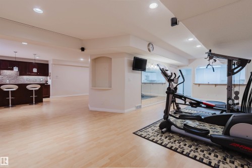 Spacious lower level featuring light wood-finish flooring, recessed lighting, and a built-in wet bar with dark wood cabinetry - 928 Heacock Road Nw, Edmonton, AB - Indoor Photo Showing Gym Room