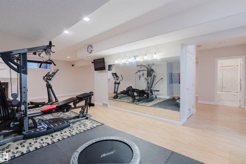 Versatile bonus room featuring light wood-finish flooring, recessed lighting, and a full-wall mirror with overhead vanity lighting - 928 Heacock Road Nw, Edmonton, AB - Indoor Photo Showing Gym Room