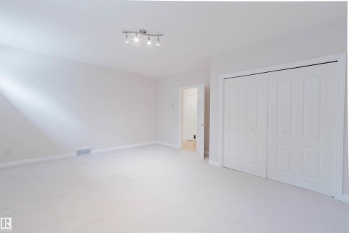 Carpeted room featuring white walls, a track light fixture, and a white bi-fold closet with panel details - 928 Heacock Road Nw, Edmonton, AB - Indoor