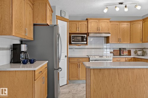Kitchen featuring light wood cabinetry, light-toned countertops, white subway tile backsplash with accent band, stainless steel appliances, and track lighting - 385 Meadowview Terrace, Sherwood Park, AB - Indoor Photo Showing Kitchen