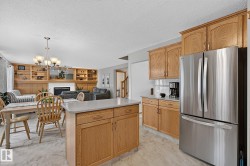 Open-concept kitchen and dining area featuring light wood cabinetry, a central island with a light-toned countertop, stainless steel appliances, and light marble-patterned flooring - 