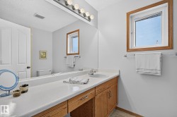 Bathroom vanity in the ensuite featuring a long countertop with an integrated sink, light wood-finish cabinetry, and a full-width mirror - 