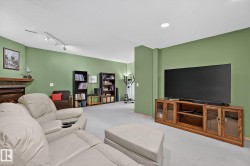 Spacious recreation room featuring light-colored carpet flooring, recessed lighting, and a prominent media console with glass-fronted cabinets - 