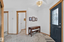 Entryway featuring a dark paneled door with decorative glass inserts, natural wood trim, a decorative ceiling light fixture, and marble-look flooring - 