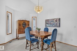 Dining area featuring a vaulted ceiling with a decorative chandelier, light-colored carpeting, and wood-trimmed windows - 